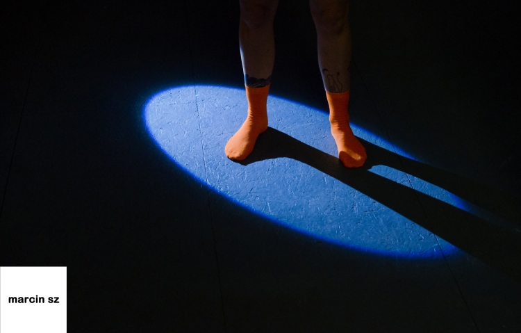 Two feet wearing orange socks stand in a single spotlight.